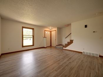A room with wooden floors and a staircase leading to another room.